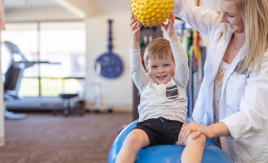 child sitting on stability ball and working with therapist