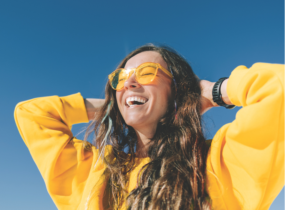 Woman smiling while wearing yellow sweatshirt and sunglasses